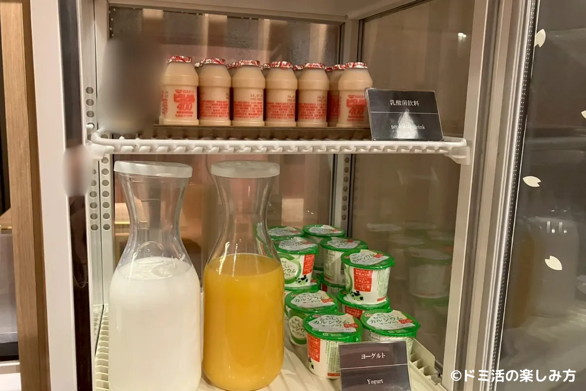 ドーミーインEXPRESS目黒青葉台の無料軽食コーナーの冷蔵ショーケースに並ぶドリンクとヨーグルトの写真